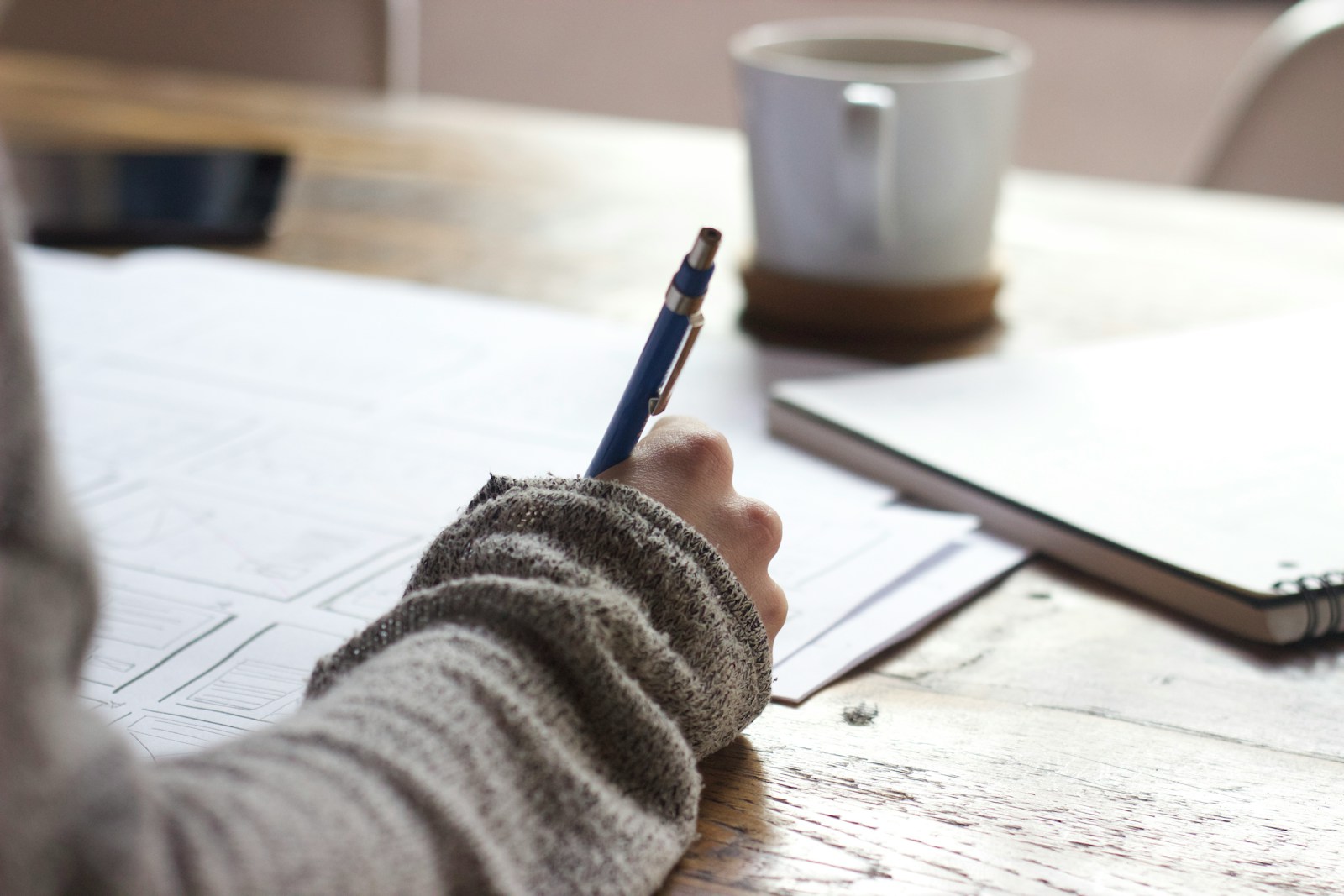 moving to dubai packing list: person writing on brown wooden table near white ceramic mug